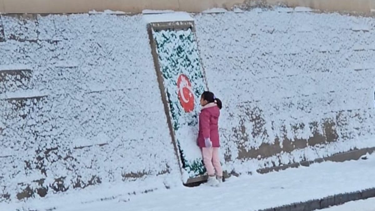 Mezarlık duvarındaki Türk bayrağı motifinin üzerine biriken karı elleriyle temizleyip